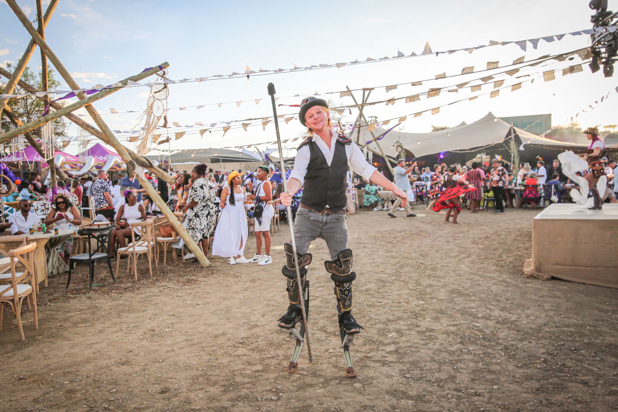 Performer dancing on stage with orange flags at sunset, festival audience seated in background