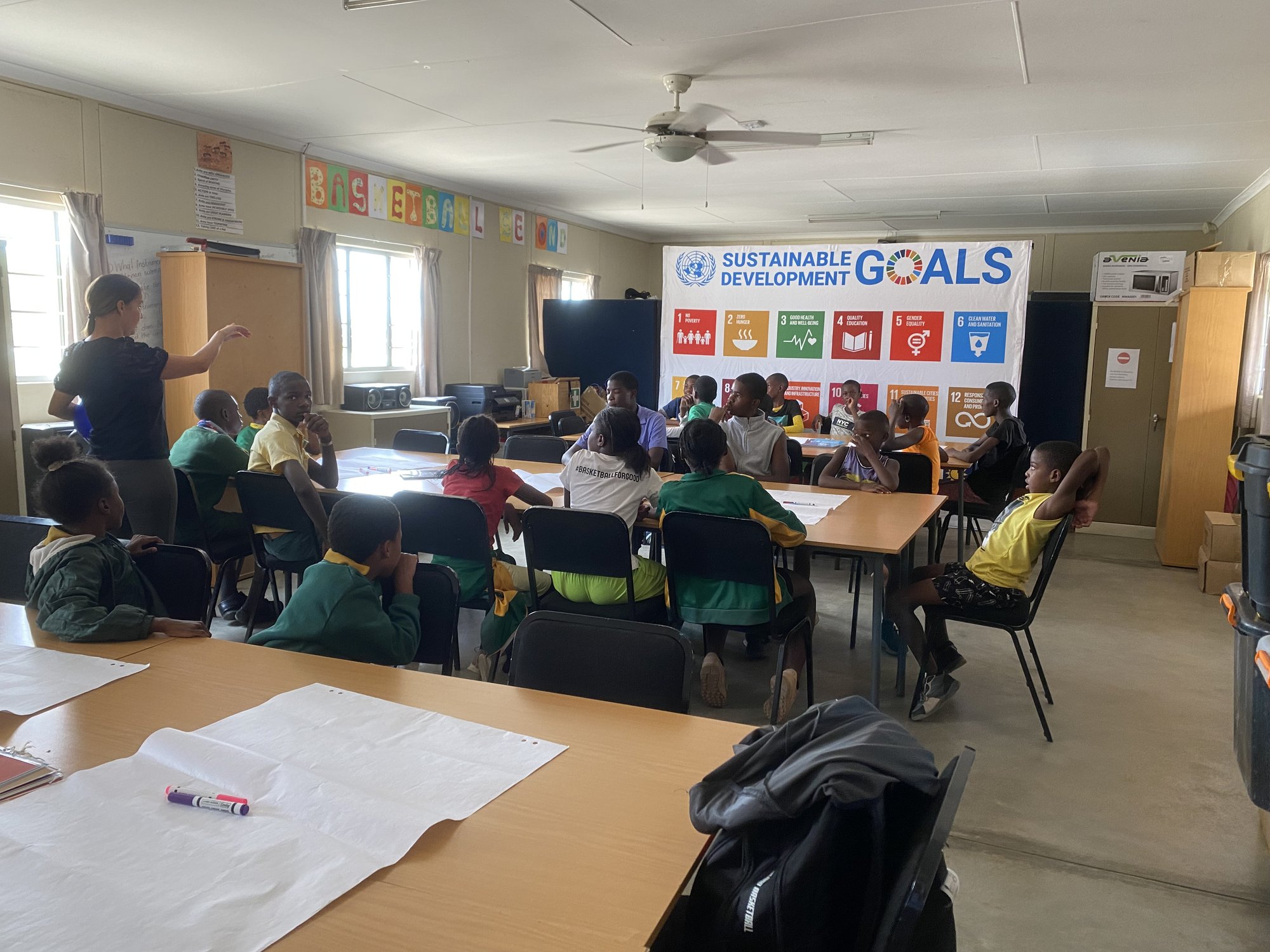 Children gathered in a classroom with a Sustainable Development Goals banner